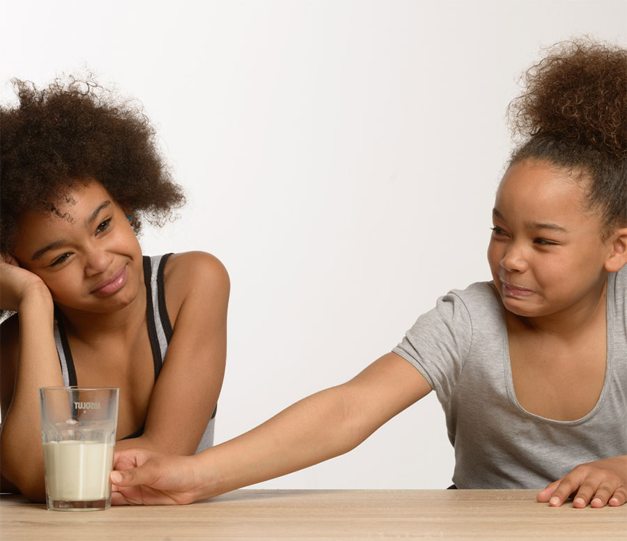 Two girls not liking a glass of milk as a metaphor for dairy intolerance